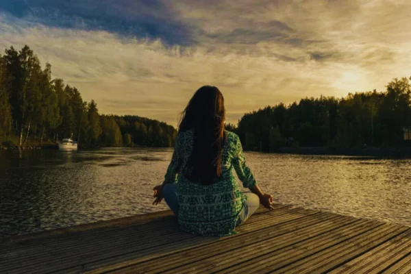 Mujer meditando frente al lago durante el atardecer para mejorar su salud mental